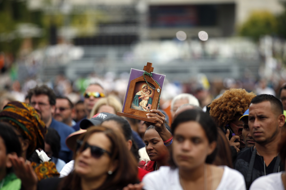 A woman holds an icon while she watches Pope Francis celebrate Mass on a large video monitor as people await the arrival of the pope at Independence Hall on Saturday in Philadelphia.