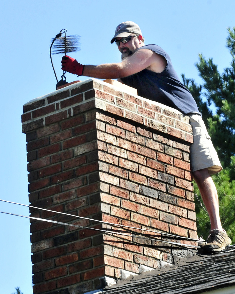 John Beane, of Complete Property Care Management Services, lifts a weighted chimney brush to clean a homeowner’s chimney.