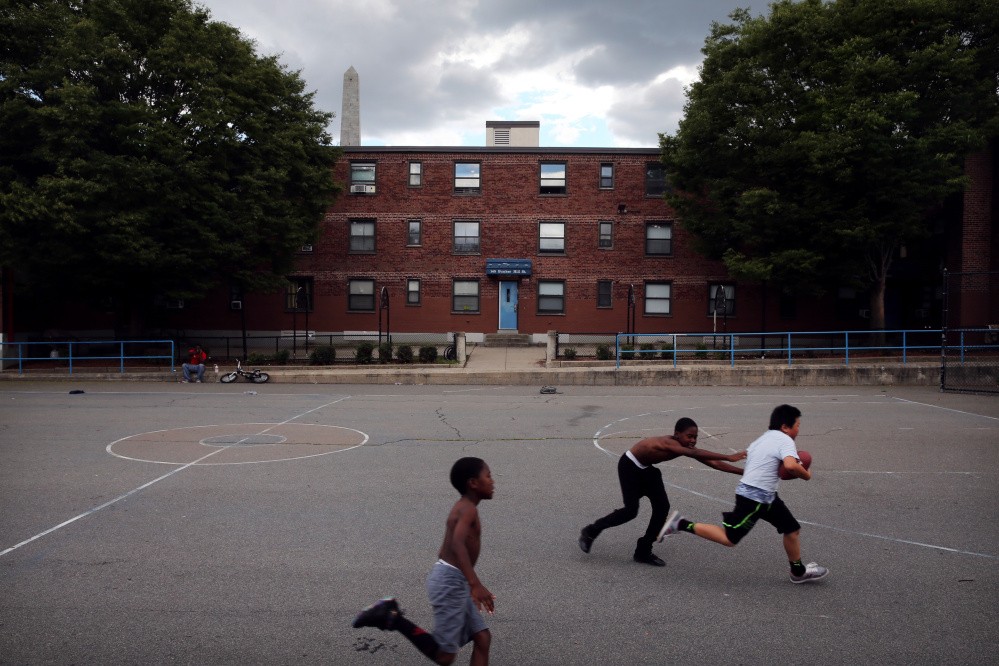 From left, Jewelz Riley and his brother David play football with Evan Yang at the Bunker Hill Development in Charlestown, Mass. Boston will allow development firms to build market-rate apartments if they are willing to build new homes for Bunker Hill’s 2,600 residents.