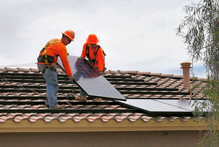 Electricians install solar panels on a roof for Arizona Public Service company in Goodyear, Ariz. Traditional power companies are getting into small-scale solar energy and competing for space. The Associated Press
