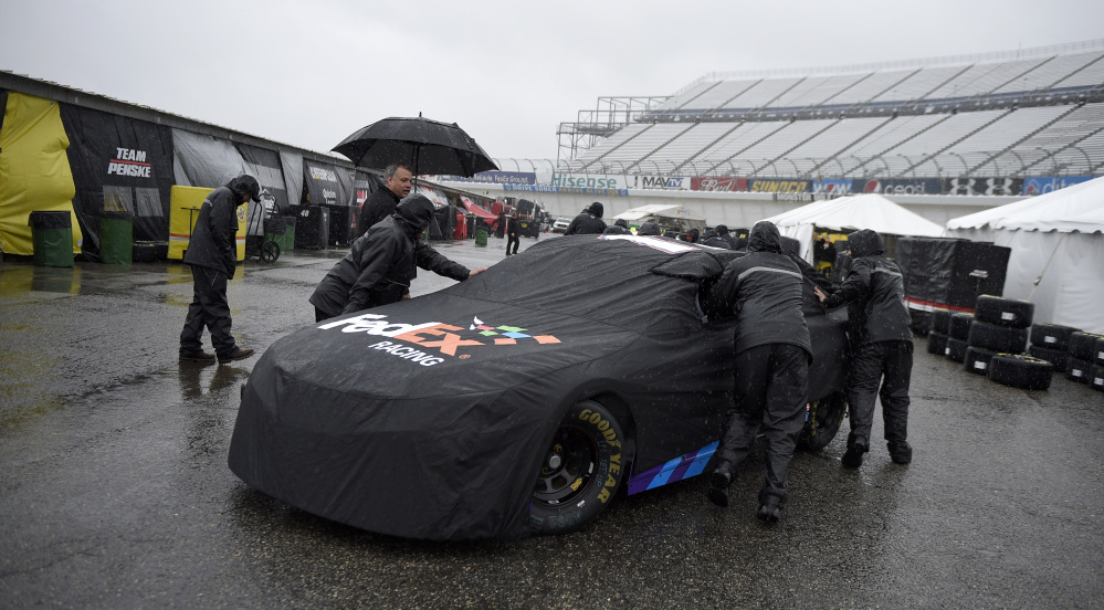 Crew members push Denny Hamlin’s car into the garage on a rainy day in Dover, Del. Qualifying for Sunday’s Sprint Cup race was canceled because of the rain, and Matt Kenseth will start on the pole.