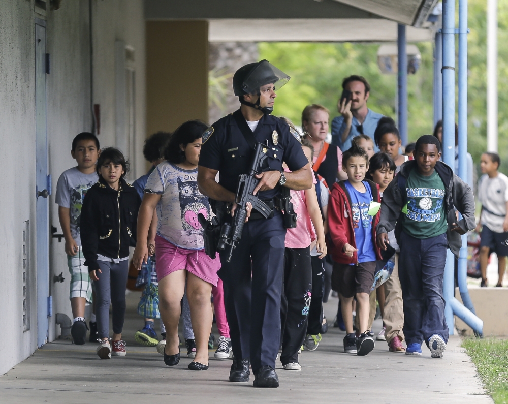 As school shootings continue, scenes such as this one are also more familiar. On June 7, 2013, an armed police officer leads young visitors away from California’s Santa Monica College following a shooting in the area. Six people were killed in the incident, including suspected gunman John Zawahri.