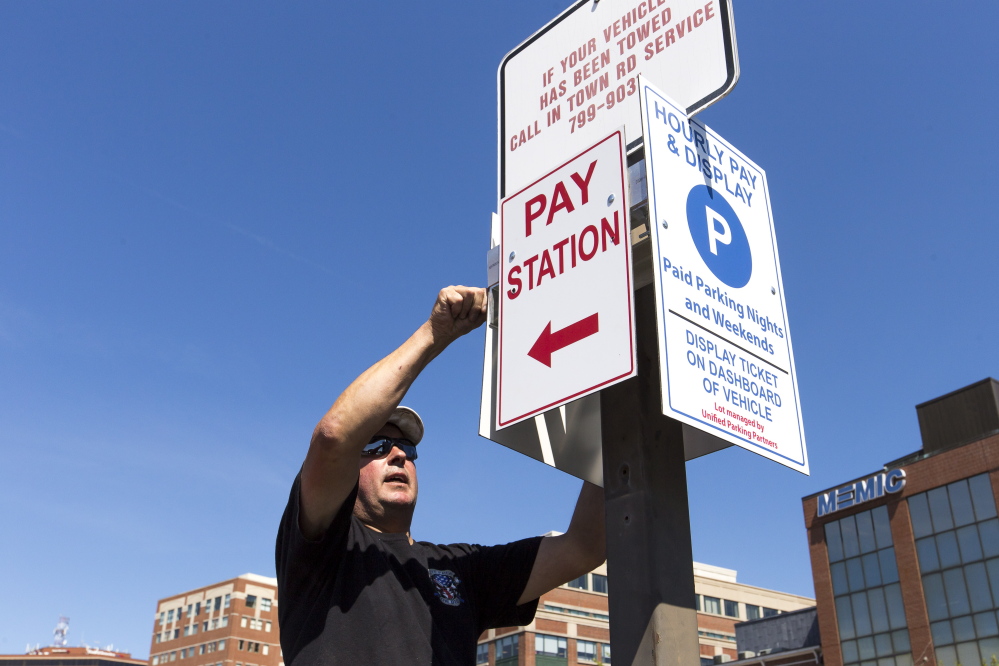 Ed Gagne installs signs last month at a private parking lot in Portland managed by Unified Parking Partners. The company has been under fire for its car-booting practices, but officials say their policy is fair and clearly spelled out.