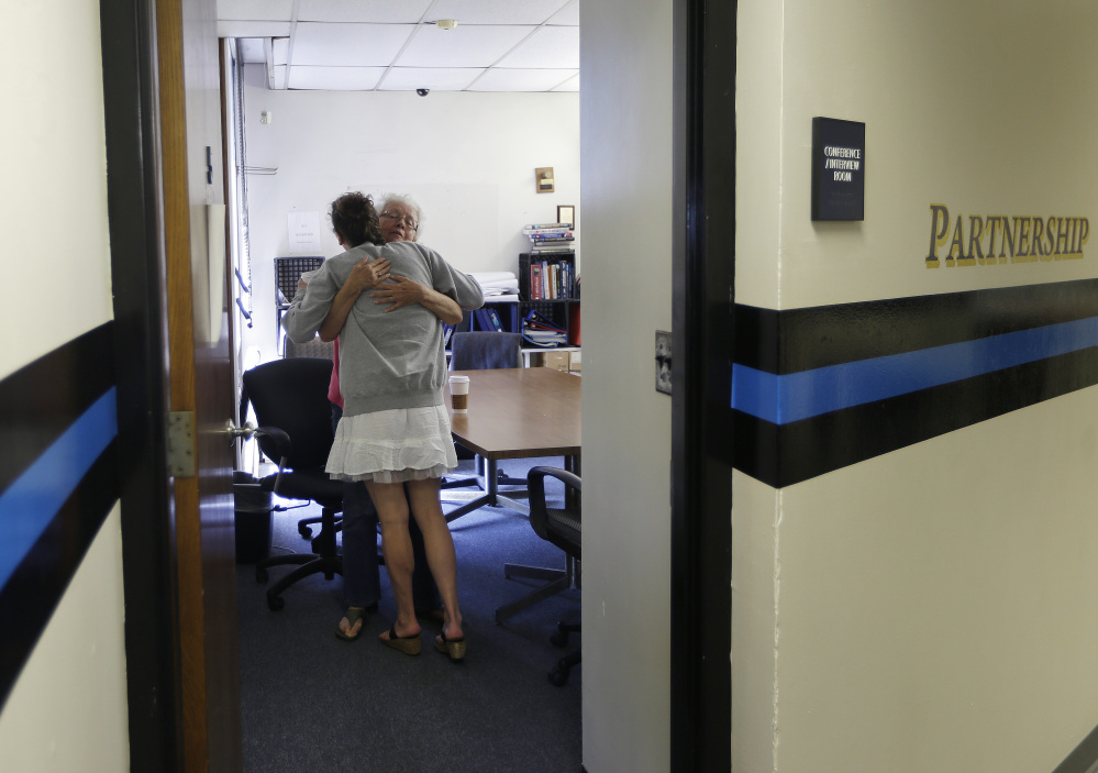 In the police station in Gloucester, Mass., in July, volunteer Ruth Cote, facing camera, hugs a participant in the Angel program, which refers drug addicts to treatment instead of prosecuting them. It’s reportedly helped nearly 200 people embark on substance-abuse recovery in Massachusetts, but will it work in Maine, a state with far fewer treatment resources?