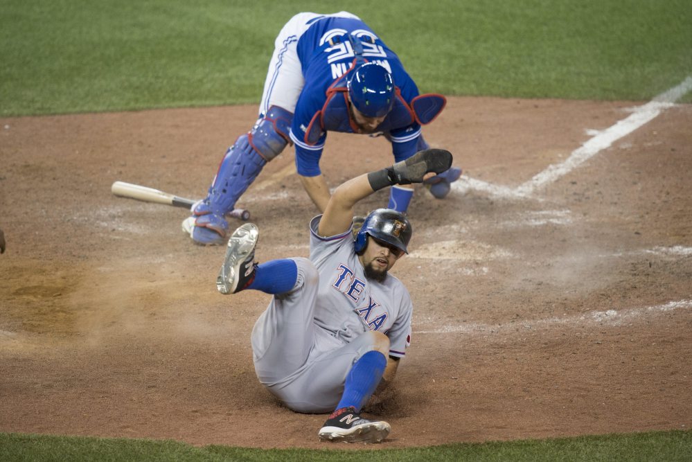 Odor slides safely past the tag of Blue Jays catcher Russell Martin to score in the 14th inning.