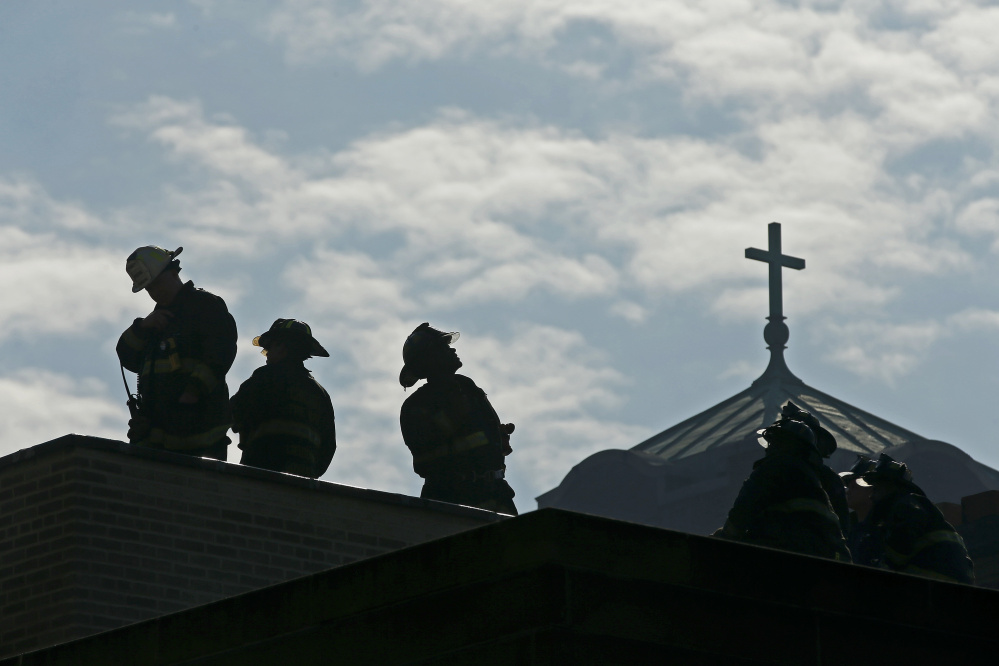 Chicago firefighters stand on a building next door to the Shrine of Christ the King Church at 64th Street and Woodlawn Avenue in Chicago as crews clean up and hose down the building on Wednesday. Jose M. Osorio/Chicago Tribune/TNS