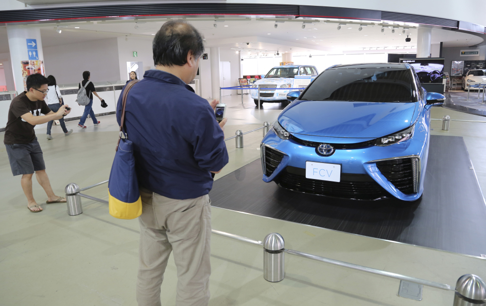 Visitors look at Toyota Motor Corp.’s new fuel cell vehicle on display at a Toyota showroom in Tokyo in June 2014. Toyota, under ambitious environmental targets, is aiming to sell hardly any regular gasoline vehicles by 2050, only hybrids and fuel cells, to radically reduce emissions.