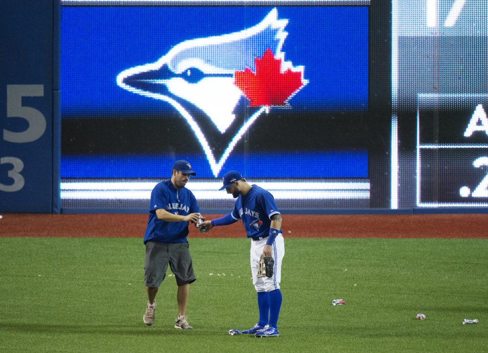 Kevin Pillar of the Blue Jays hands beer cans to a member of the grounds crew during an outburst by Toronto fans in the seventh inning after the umpires awarded Texas a disputed run.