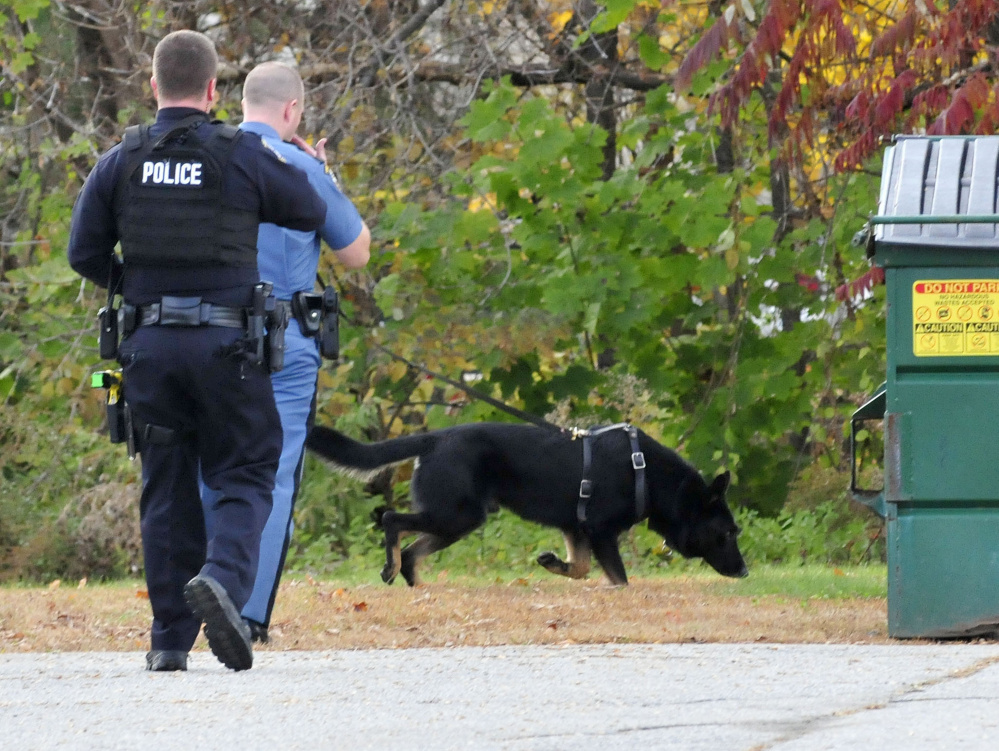Waterville police Officer Cameron Huggins, left, and a state trooper with a tracking dog search for the man who robbed the Rite Aid store on Main Street in Waterville on Thursday.