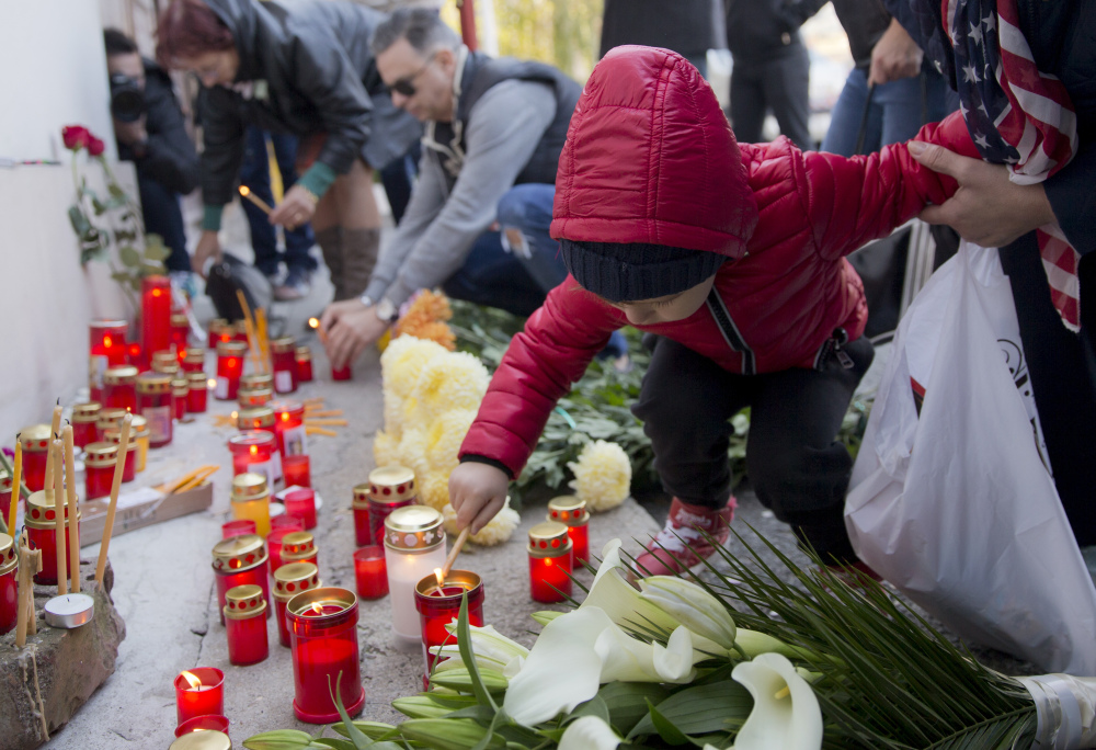 A child lights a candle outside the nightclub in Bucharest, Romania, where a fire and panic claimed the lives of 27 people.