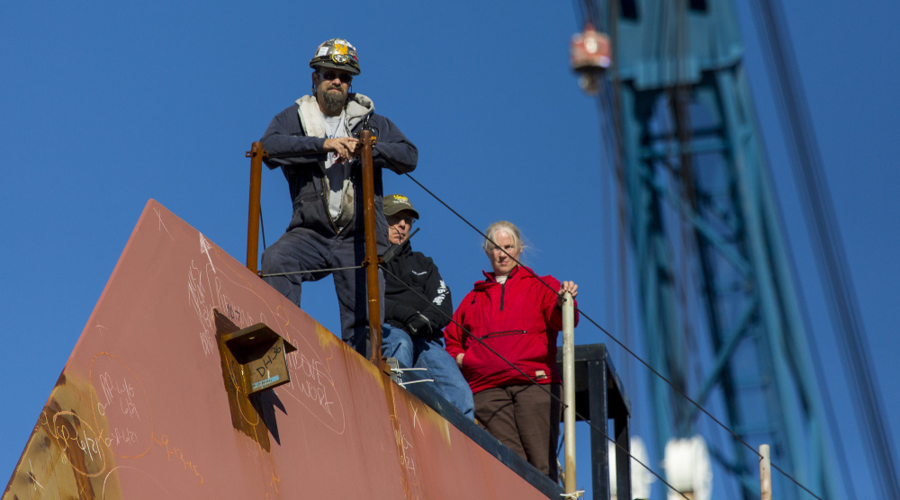 Production workers at Bath Iron Works stand on the bow of the in-progress USS Michael Monsoor during a christening ceremony Saturday. Workers are being pulled off projects to work on the USS Zumwalt, which is a year behind schedule.