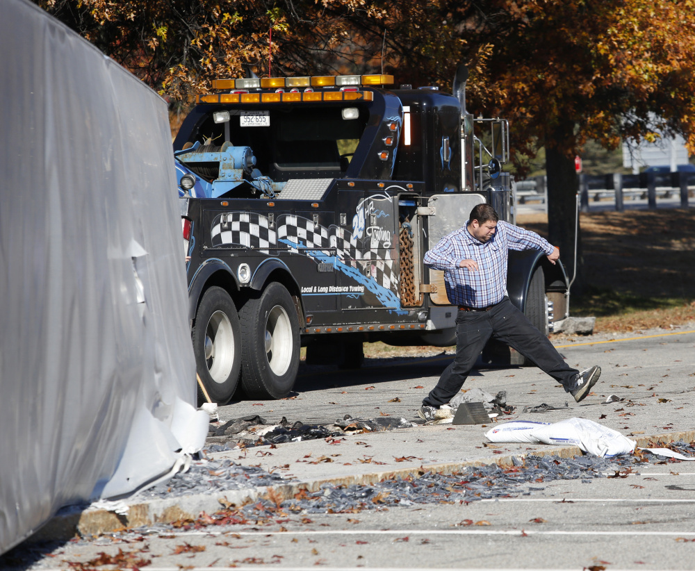 The driver of a tractor-trailer that overturned at the northbound service plaza off the Maine Turnpike in Kennebunk on Monday steps over debris while clean-up crews work at the scene.