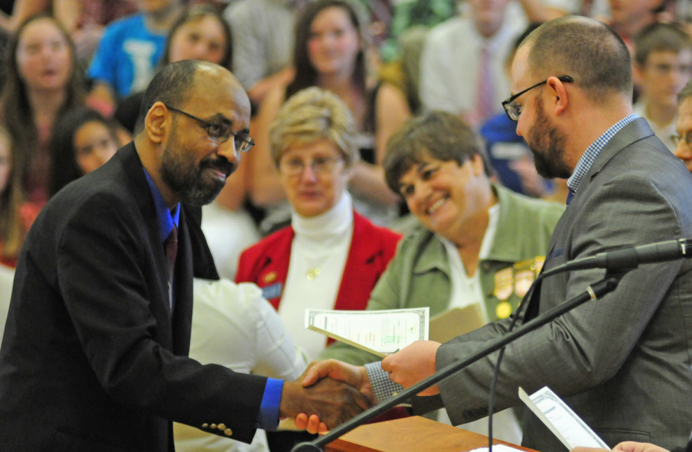 Ali Mohamed, of Auburn, left, shakes hands with Immigration Services Officer Ryan Locke as he receives a certificate during a naturalization ceremony Friday at Maranacook Community Middle School in Readfield.