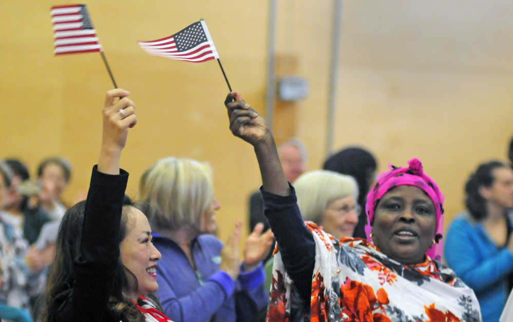 New citizens Chau Do, left, and Marion Mohamed, both of Lewiston, wave American flags after a naturalization ceremony Friday at Maranacook Community Middle School in Readfield.