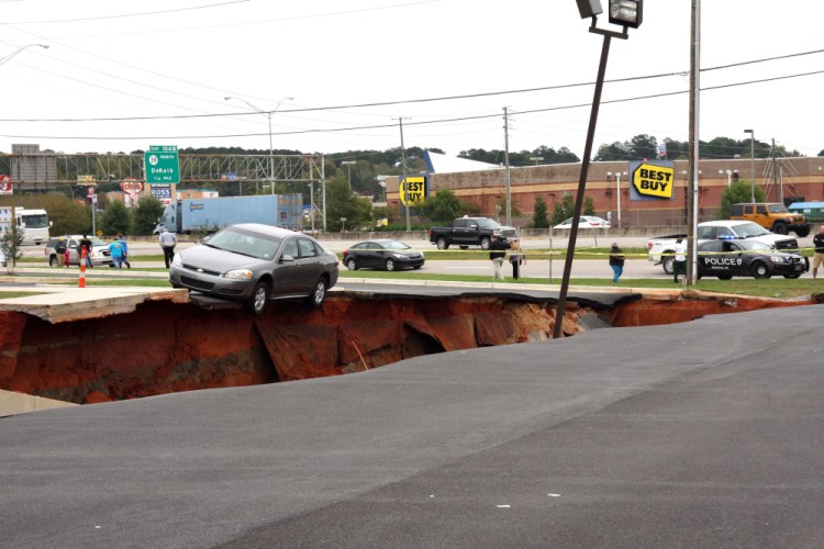 A car teeters on the edge of a cave-in of a parking lot in Meridian, Miss., on Sunday.