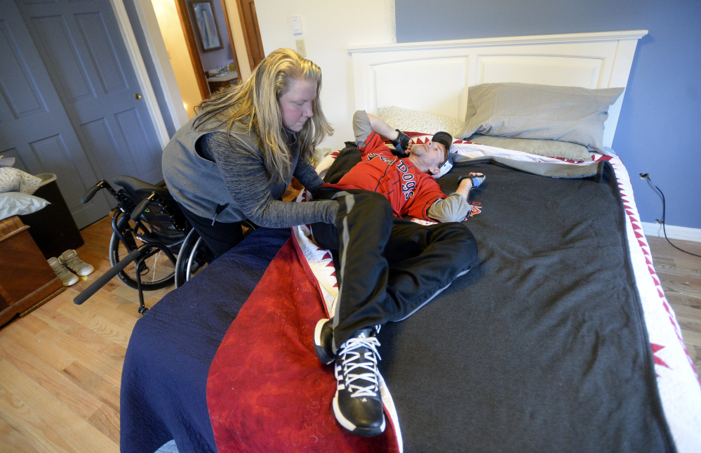 Carrie Walker helps her husband, Brian, who was paralyzed after a four-wheeler accident, as he gets in bed to work on some exercises to strengthen his neck and shoulders at his Portland home last December.