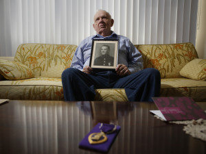 At his home Monday in Portland, John “Jack” Whitney holds a photograph of his older brother, Marine Pfc. Thomas Whitney, one of thousands of military personnel missing from World War II and other conflicts. In the foreground is Thomas Whitney’s Purple Heart.
