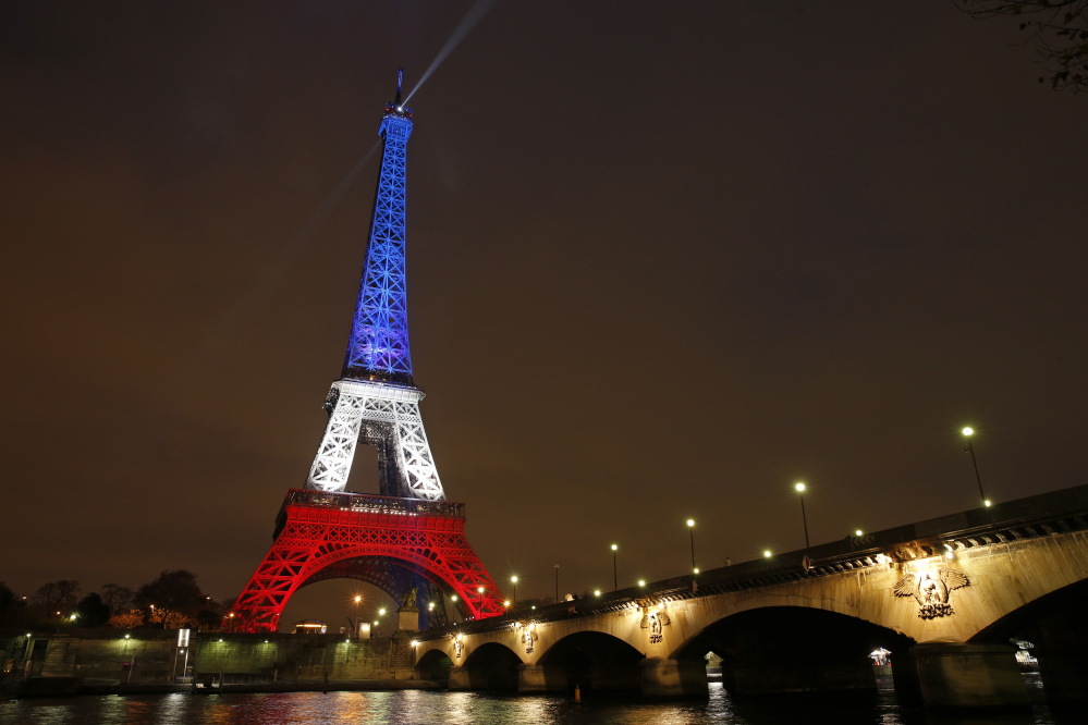 The Eiffel Tower is bathed in floodlights displaying the colors of the French flag Monday as thousands gathered there and in the Place de la Republique square around memorials to the victims of Friday’s attacks.