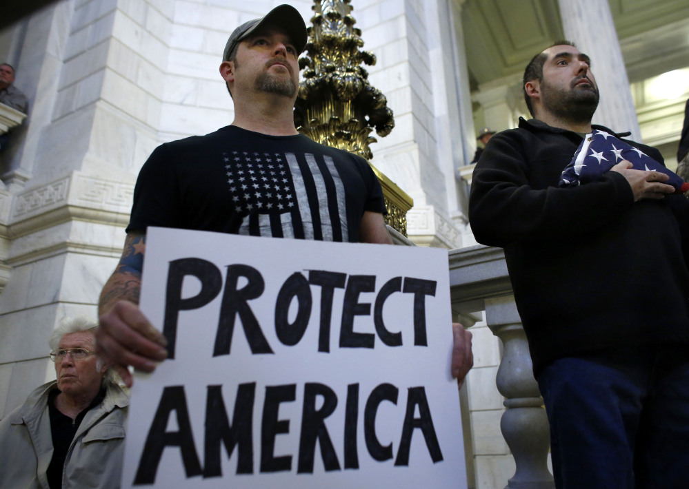 Army veteran Jim Purcell of Burrillville, R.I., front left, displays a placard as Navy veteran Robert Martinez, right, holds a folded American flag during a rally Thursday at the Statehouse in Providence, R.I. The demonstrators oppose allowing Syrian refugees to enter Rhode Island following the terror attacks in Paris.