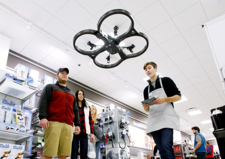 Cary Grimmett, left, and Kaylei Combs watch as Brookstone employee Dylan Crovo demonstrates the flying capabilities of a drone at the Maine Mall in South Portland.