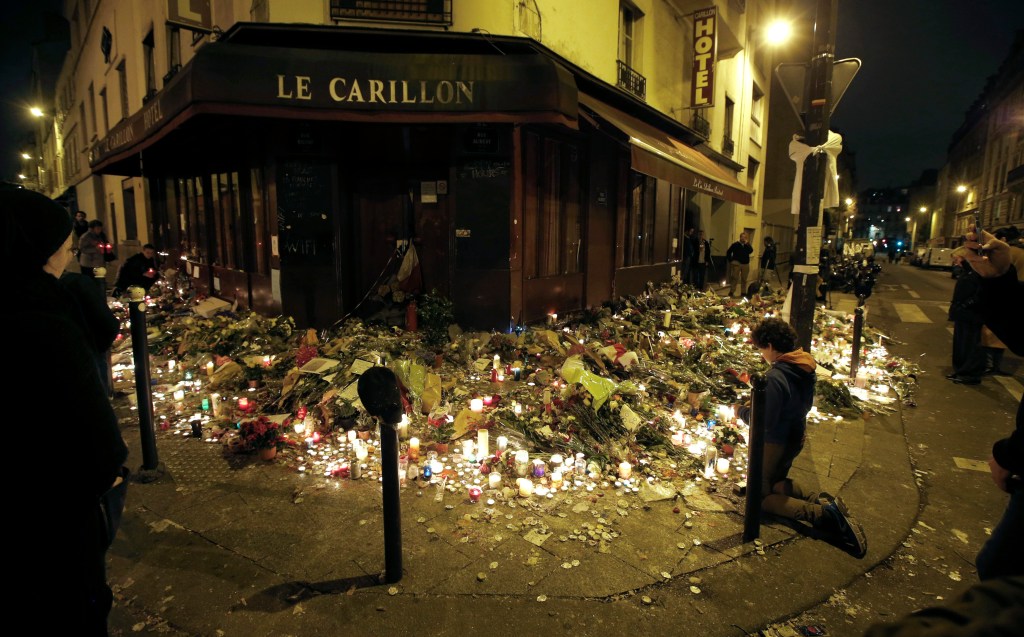 People pray Sunday outside Le Carillon restaurant, one of the attack sites where crowds have laid flowers and lit candles in memory of the 15 people killed there. At one point jittery mourners panicked and police moved in with guns drawn.  Jacky Naegelen/Reuters