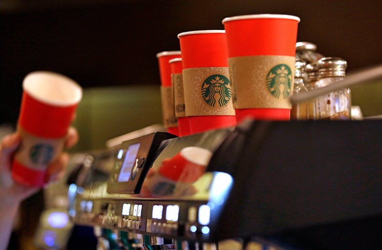 A barista reaches for a red paper cup as more, with cardboard sleeves attached, line the top of an espresso machine at a Starbucks coffee shop in Seattle. Starbucks' minimalist new holiday coffee cup has set off complaints that the chain is making war on Christmas. 
