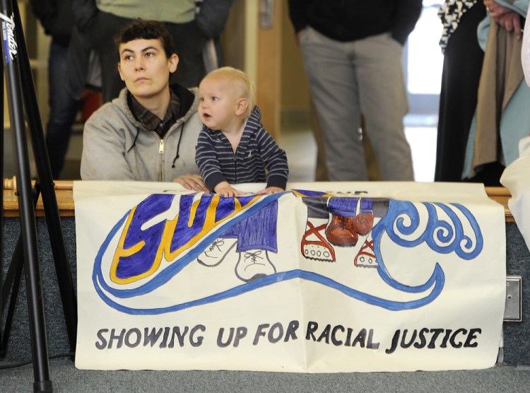 Christine Baglieri, with Showing Up for Racial Justice, Central Maine Chapter, awaits her turn to speak as she sits with a friend’s child, Jackson, behind a banner at a rally to stand together against institutional racism, at the Woodbury Center at the University of Southern Maine on Wednesday.