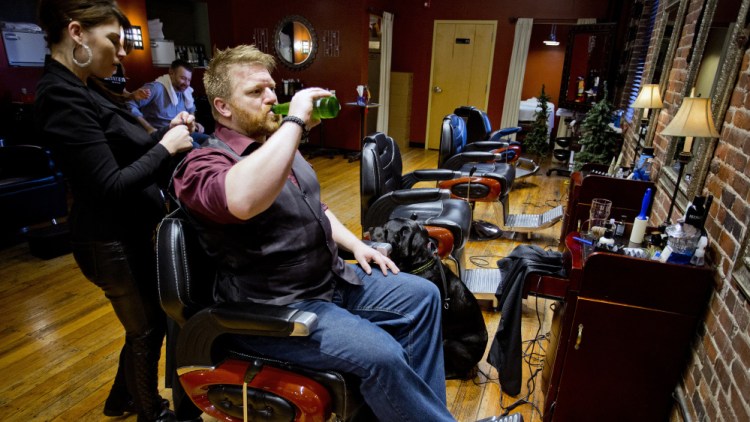 Fred Twombly drinks a beer with his dog, Milo, at his side as Christina Bailey prepares to cut his hair at Mensroom Salon & Lounge in Portland. Mensroom, which has operated in Portland for more than a decade, is part of a business segment that seems to be growing in popularity: a place to get your hair cut while having a beer and maybe shooting a round of pool.