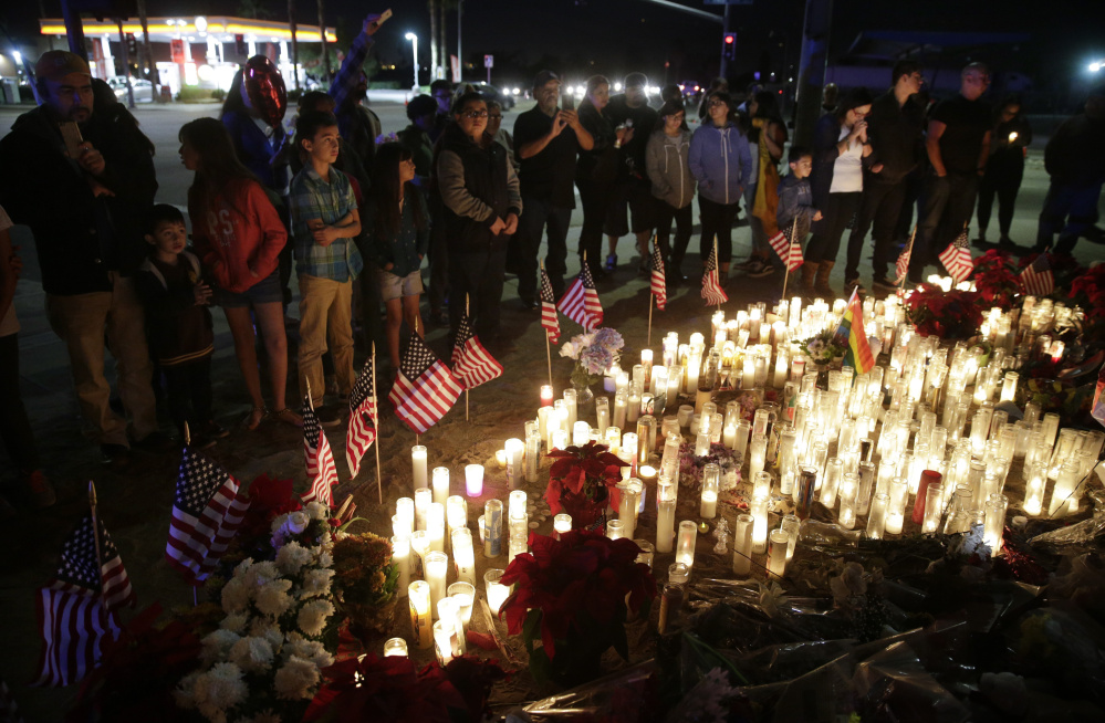People pay respects to last week’s shooting victims Sunday evening at a makeshift memorial in San Bernardino, Calif. Also Sunday, authorities searched the home of a of a man suspected of providing shooter Syed Rizwan Farook with guns.