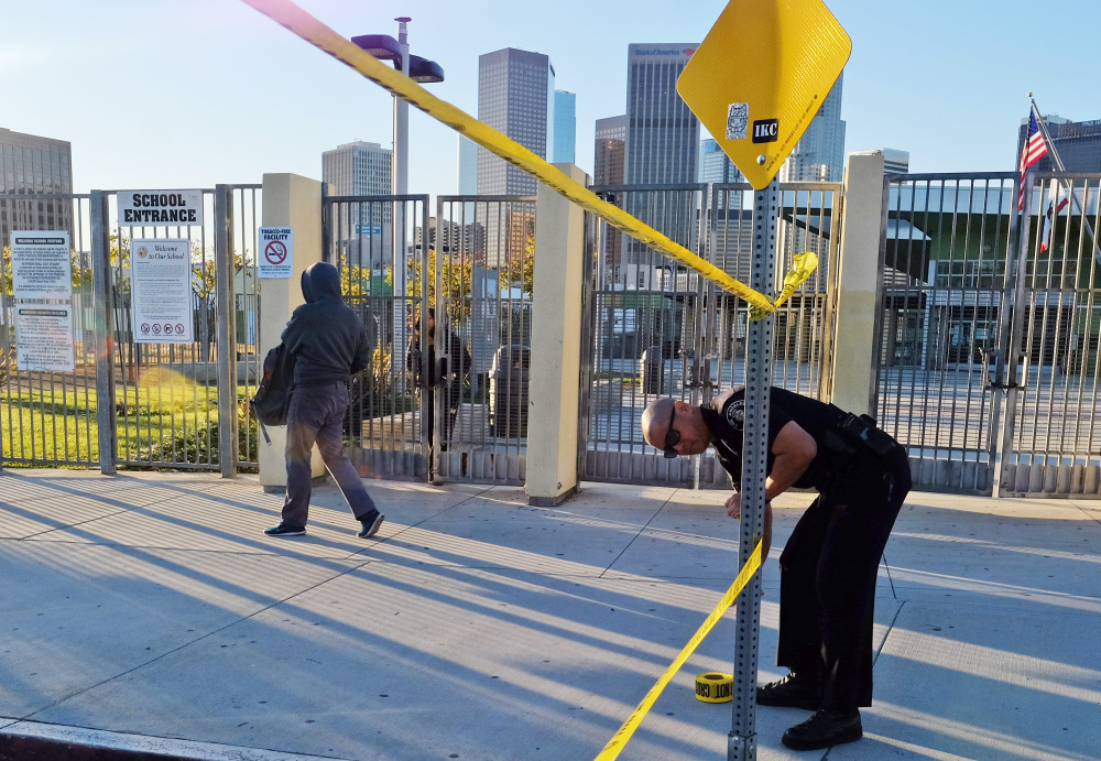 A police officer puts up yellow tape to close the school as a student walks past Edward Roybal High School in Los Angeles on Tuesday.