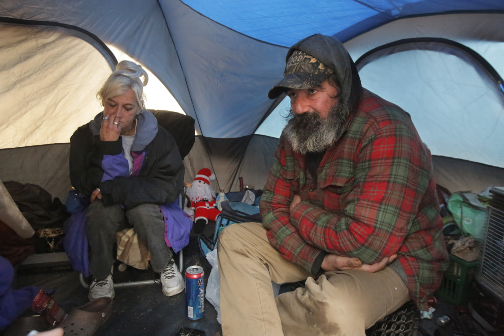 Sherri Ferrier and Jamey Wade spend time on a rainy Thursday in Ferrier’s propane-heated tent in the woods on the outskirts of Portland, where Wade also has a tent. Ferrier was not displaced by the state’s brush-clearing project along Interstate 295 but says she has had her camps torn down in the past. “It’s sad because they’re taking everything away from us,” she said.