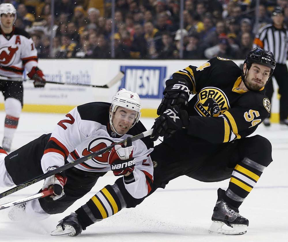 New Jersey’s John Moore, left, gets tangled up with Boston’s Adam McQuaid during their game Sunday in Boston. The Bruins scored in the first period, then beat the Devils in a shootout and are 11-1-3 in their last 15 games.