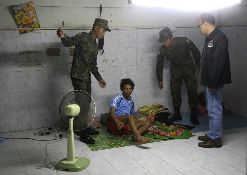 In this Monday, Nov. 9, 2015 photo, Thai soldiers and a member of the Department of Special Investigation wake up a worker during a raid on a shrimp shed in Samut Sakhon, Thailand.