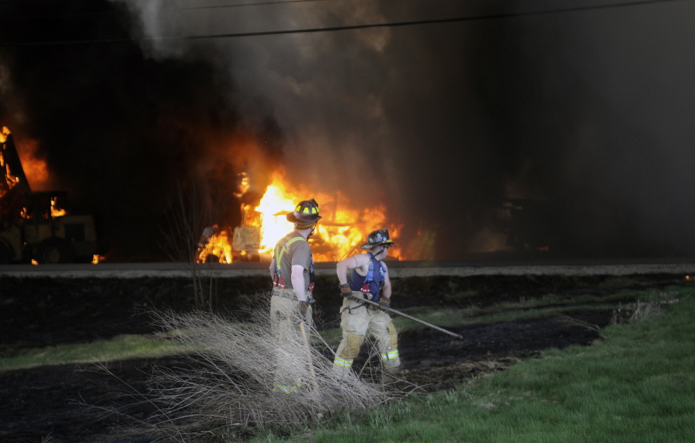 Firefighters extinguish a brush fire from an explosive blaze that destroyed AD Electric Inc.’s warehouse in Monmouth in May. The original $21,600 fine was reduced on appeal.