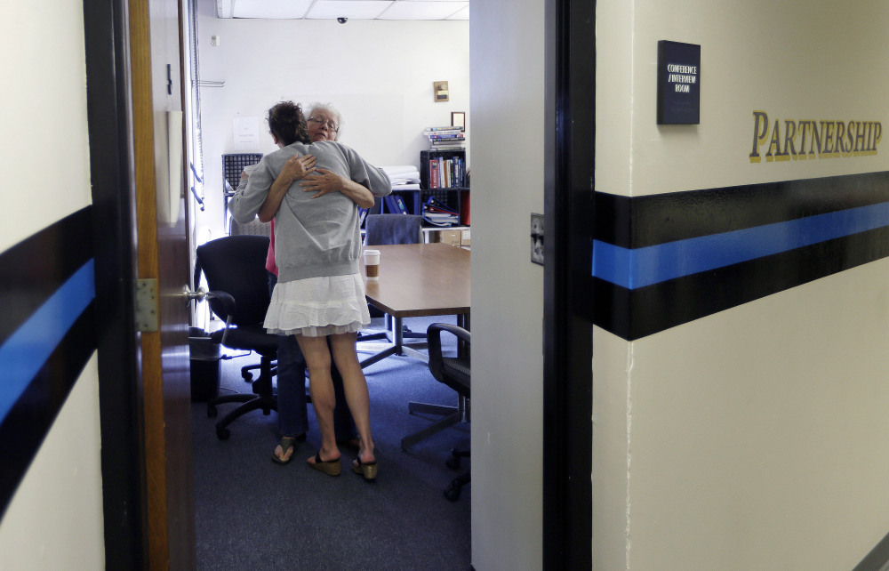 Kylee Moriarty, facing away, hugs volunteer Ruth Cote in the police station in Gloucester, Mass. In July, Moriarty became one of the first to benefit from the Gloucester Police Department’s policy of helping addicts get treatment instead of jailing them.