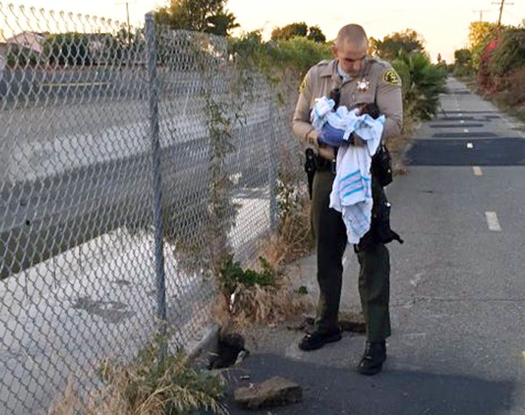 Deputy Adam Collette holds an infant girl found abandoned under asphalt and rubble near a bike path in Compton, Calif., on Friday, in this photo provided by the Los Angeles County Sheriff's Department.