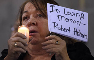 A woman holds a sign for Robert Adams, who died in a shooting on Wednesday, during a vigil for shooting victims on Thursday, Dec. 3, 2015, at San Manuel Stadium in San Bernardino, Calif. A husband and wife opened fire on a holiday banquet, killing multiple people on Wednesday. Hours later, the couple died in a shootout with police. (AP Photo/Mark J. Terrill)