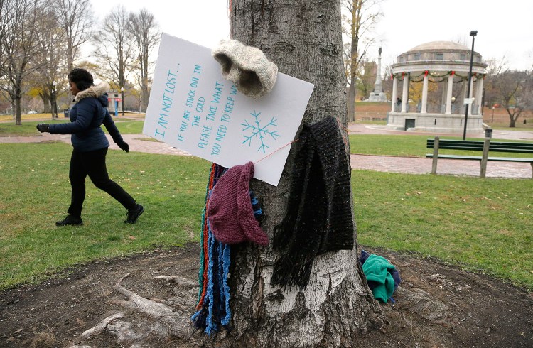 Hats and scarves hang on a tree near a sign that invites people in need to take them to keep warm, on the Boston Common on Tuesday in Boston.