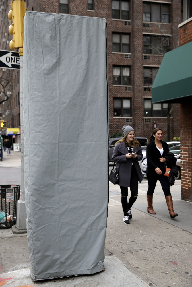 In this photo taken on Thursday, Dec. 31, 2015, women walk near a covered wireless kiosk at an intersection in New York. The 9-foot-tall, narrow structure installed this past week on a Manhattan sidewalk is signaling a plan to turn payphones into what's billed as the world's biggest and fastest municipal Wi-Fi network. The first of at least 7,500 planned hot spots are due to go online early next year, promising superfast and free Wi-Fi service, new street phones with free calling, ports to charge personal phones and a no-cost windfall for the city.   (AP Photo/Seth Wenig)