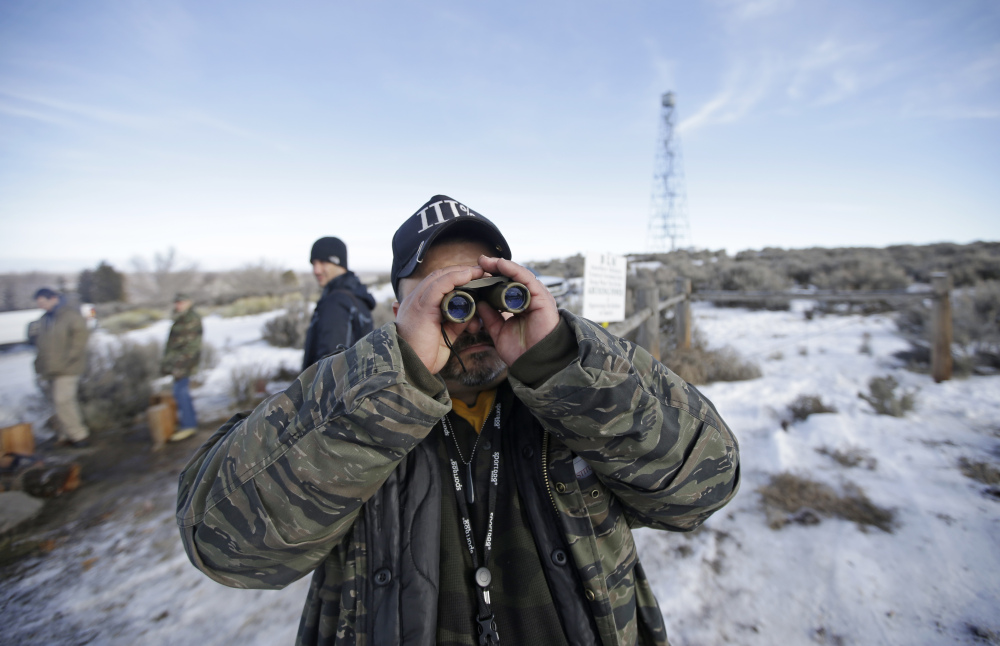 Sean Anderson, of Idaho, a supporter of the group occupying the Malheur National Wildlife Refuge, looks through binoculars at the front gate Wednesday near Burns, Ore.
