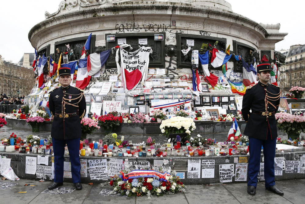 French honor guards stand next to the monument at Place de la Republique in Paris, where people laid candles, cards and flags during a ceremony Sunday to honor the victims of the Islamic extremist attacks around Paris in 2015.