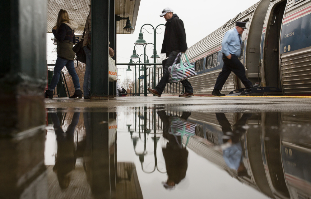 Passengers disembarking the northbound train from Boston at the Saco Transportation Center are reflected in a water puddle Sunday. Carl D. Walsh/Staff Photographer