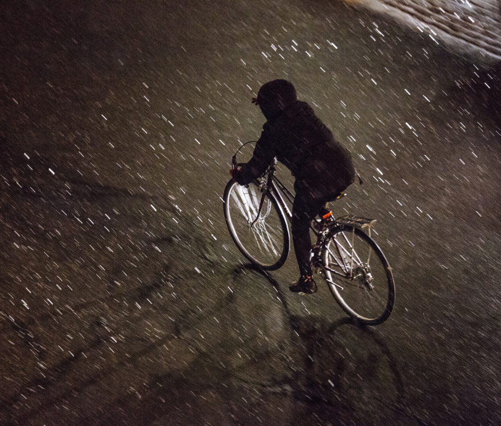 A bicycle rider navigates a slippery Free Street as snow begins to accumulate Tuesday evening, necessitating a parking ban in downtown Portland.