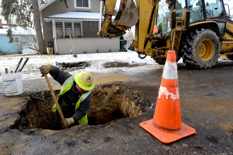 Richard Garza moves dirt around the water main after replacing the lead water pipe with a new copper one Friday at a home in Lansing, Mich.