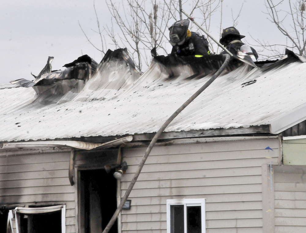 Firefighters working to extinguish a fire rip a hole in the roof of a mobile home in Athens on Tuesday.