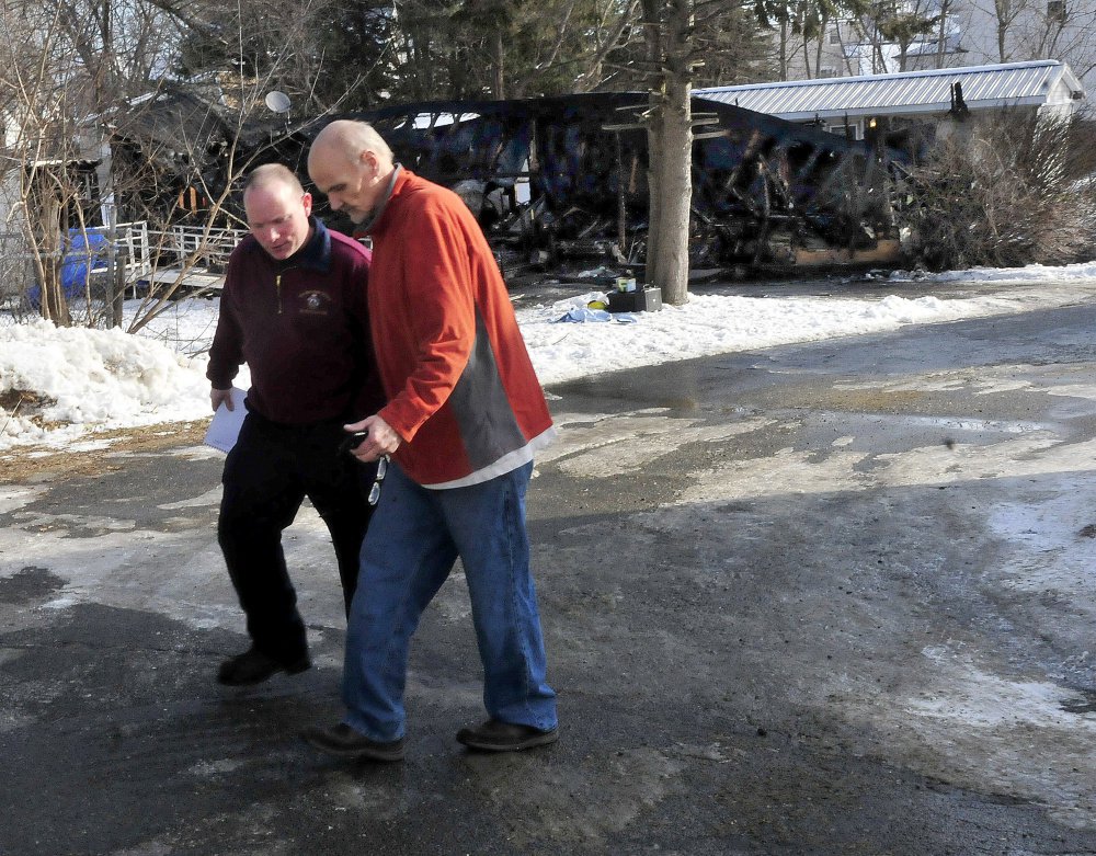 Jeremy Damren, left, of the state fire marshal’s office. interviews Bruce Cornforth beside the home where David Chamberlain died in a fire Monday in Waterville.