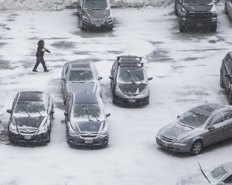 A pedestrian walks across a parking lot off Free Street as the snow begins to fall Monday afternoon in Portland.