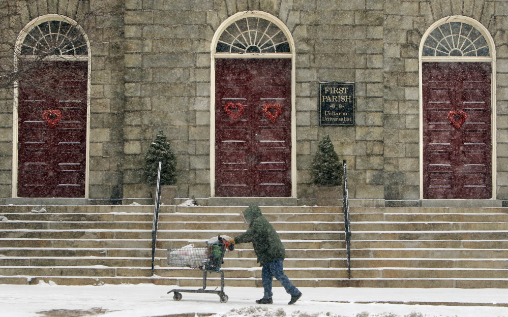 A man pushing a carriage makes his way up Congress Street past the First Parish Church through windblown snow on Monday.