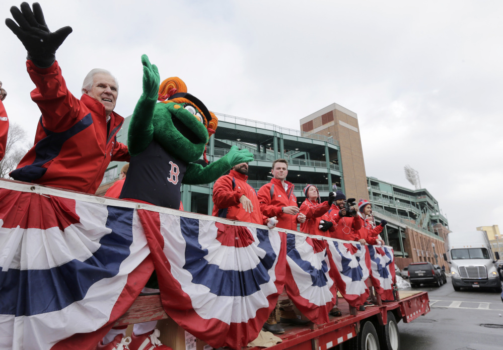 The Boston Red Sox new mascot Tessie the Green Monster, second from left, rides on the back of a truck with team ambassadors leading the team's equipment truck, behind right, as the equipment truck departs Fenway Park in Boston on Wednesday, en route to the team’s spring training baseball facility in Fort Myers, Fla. (AP Photo/Steven Senne)