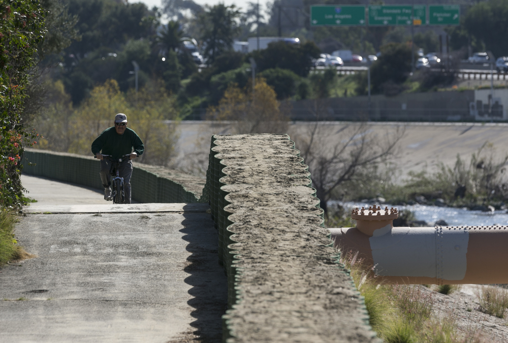 A cyclist rides along recently installed temporary flood control walls along the L.A. River in Los Angeles Friday, but the structures hardly seem necessary as much of the West Coast has just endured 10 days of record heat and no precipitation.